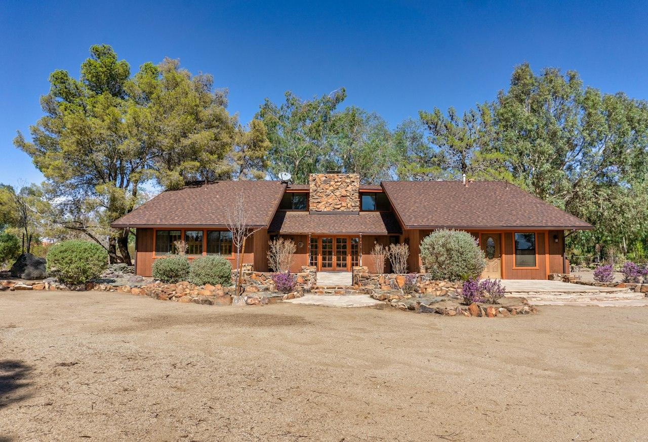 A single-story California ranch house with a low-pitched gable roof, wood siding and a stone chimney, set behind a drought-tolerant garden