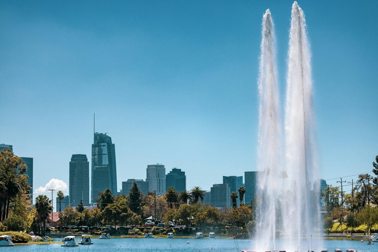 The tall fountain in Echo Park Lake with palm trees and the Downtown Los Angeles skyline beyond under a clear blue sky