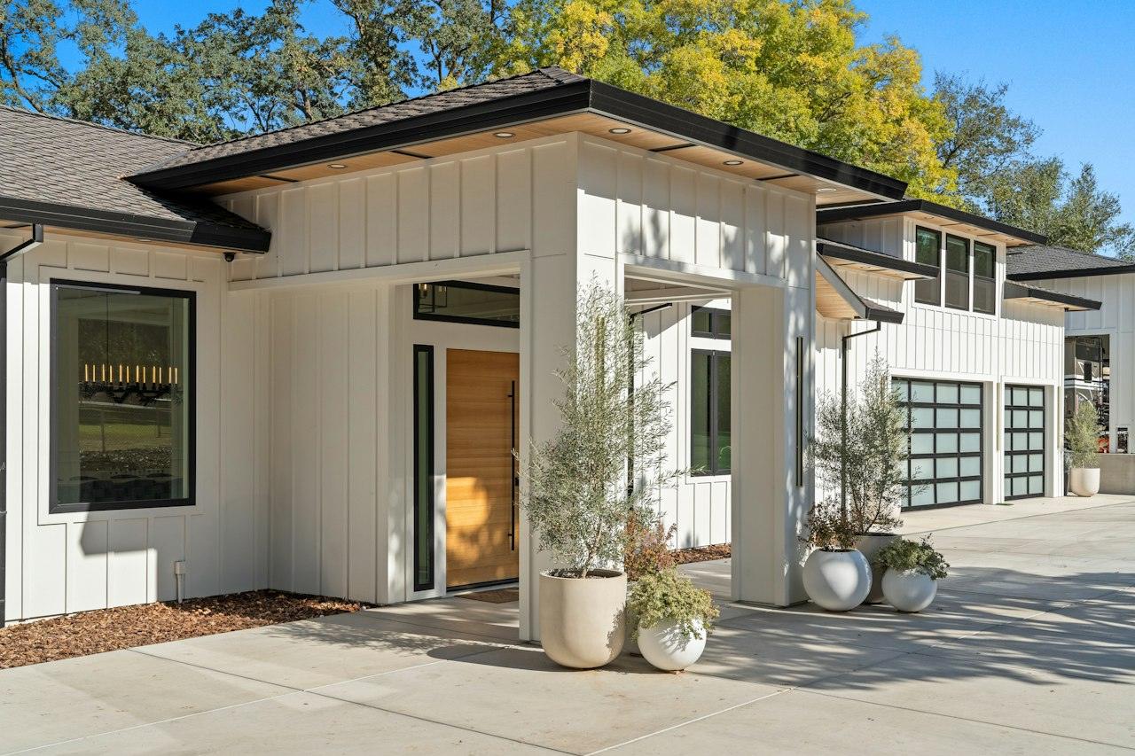 A new modern farmhouse with white board-and-batten siding, black window trim, a natural wood front door and glass garage doors