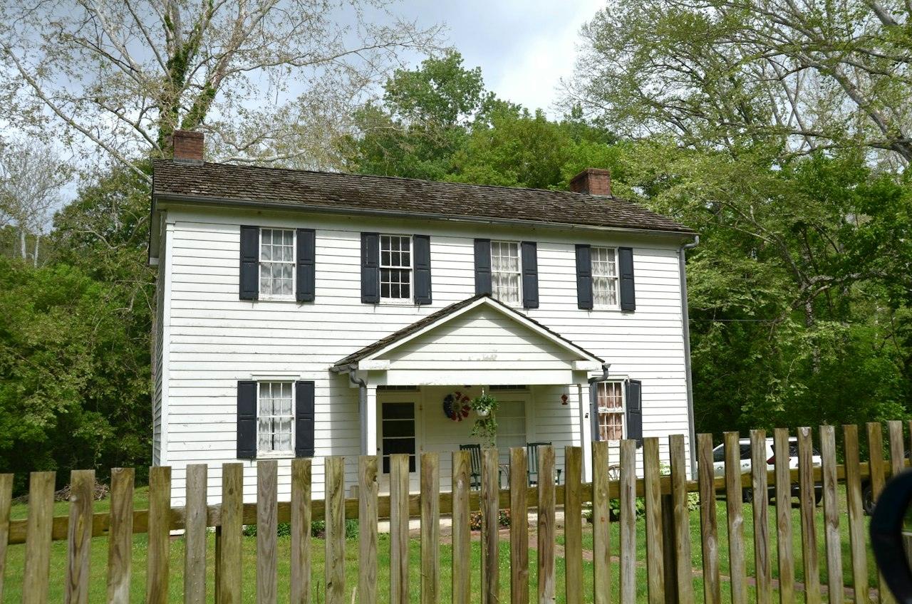 A two-story white clapboard Colonial house with black shutters, a center door under a pedimented porch and a brick chimney