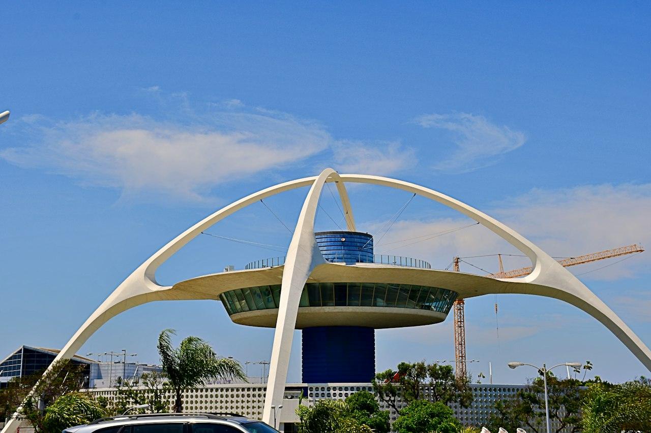 The space age Theme Building at LAX, its white arches framed against a bright blue sky with palm trees below